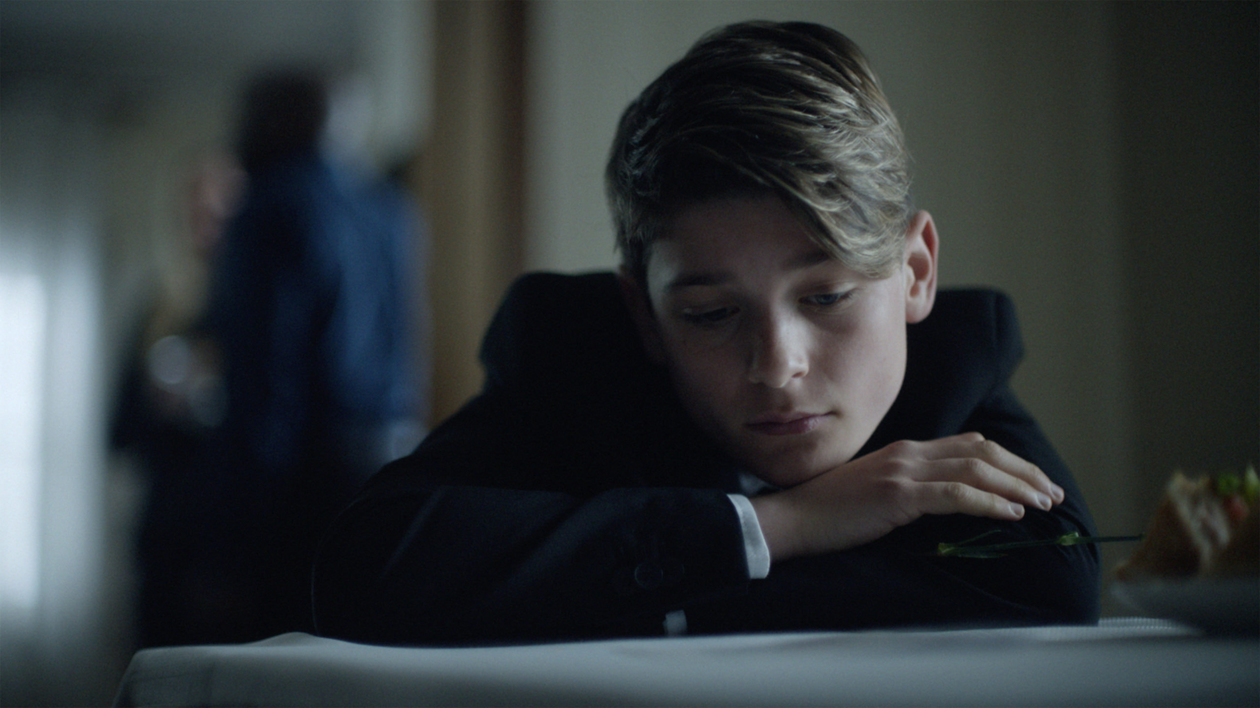 Boy in suit looking sad at a table